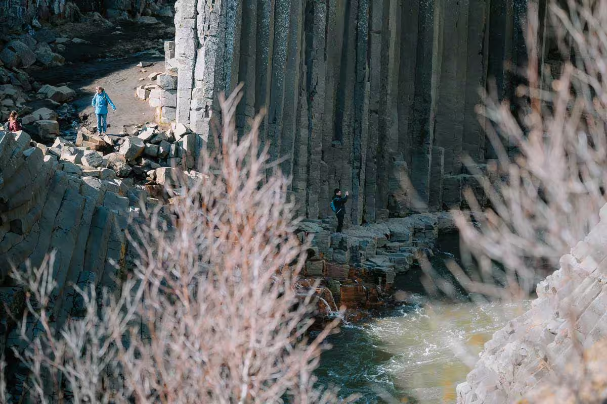Tourists exploring Studlagil Canyon's dramatic basalt columns beside a glacial river in East Iceland