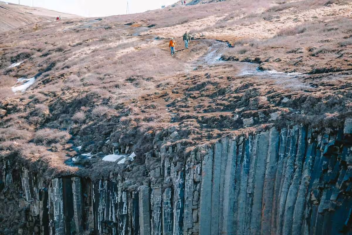 Two hikers walking along the edge of Studlagil Canyon's dramatic basalt column cliffs in Iceland