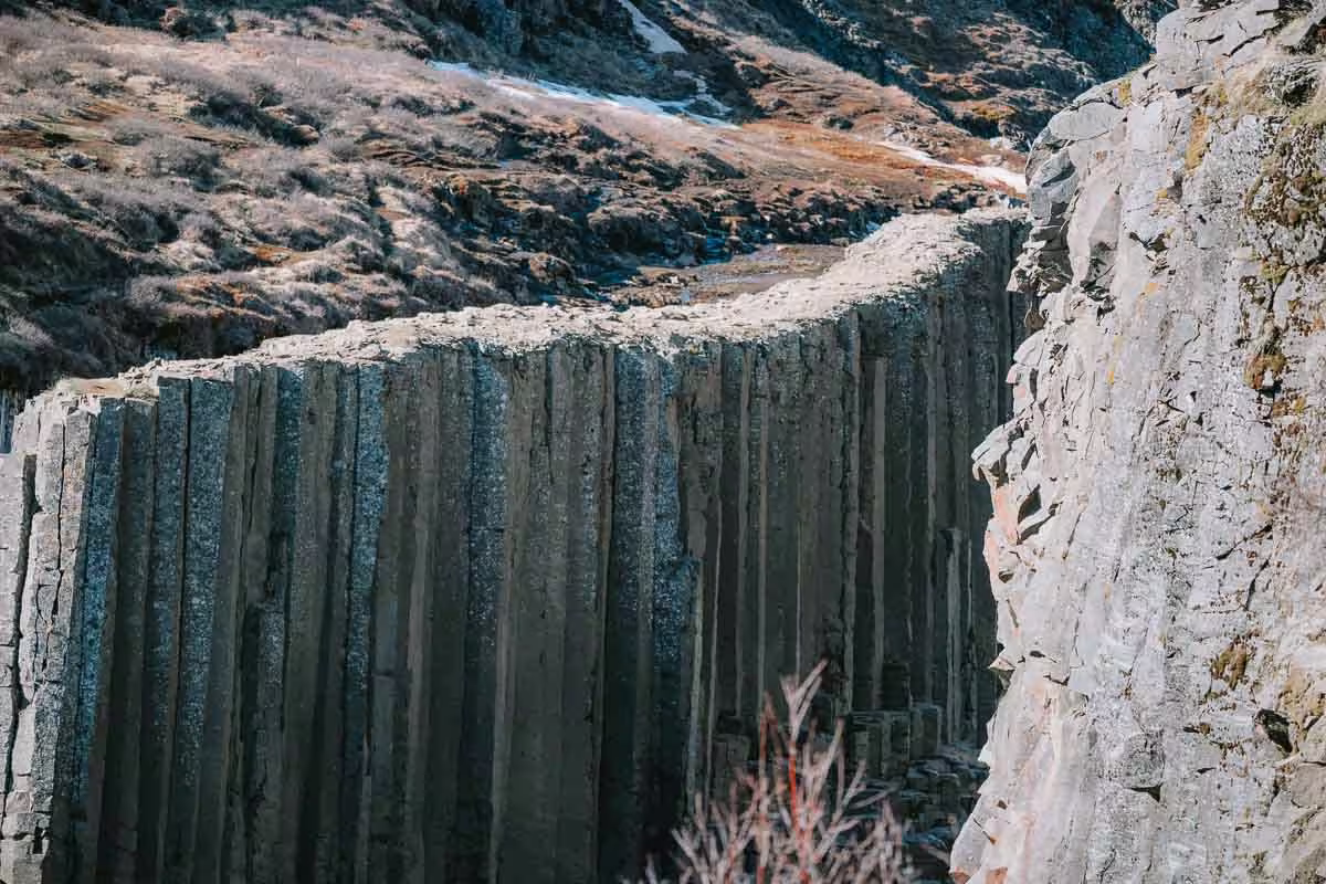 Towering dark basalt columns at Studlagil Canyon with rugged mountain landscape in background, Iceland