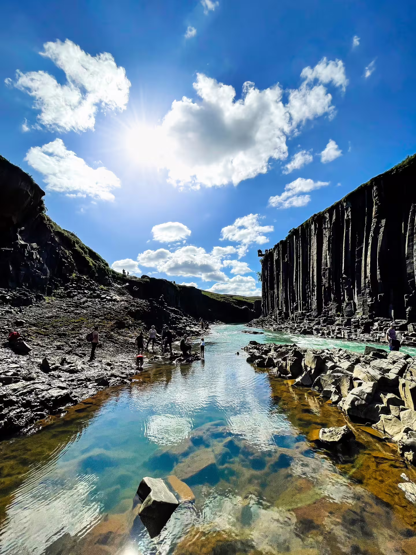 Turquoise river flowing through Studlagil Canyon with towering basalt columns and visitors exploring the rocky banks