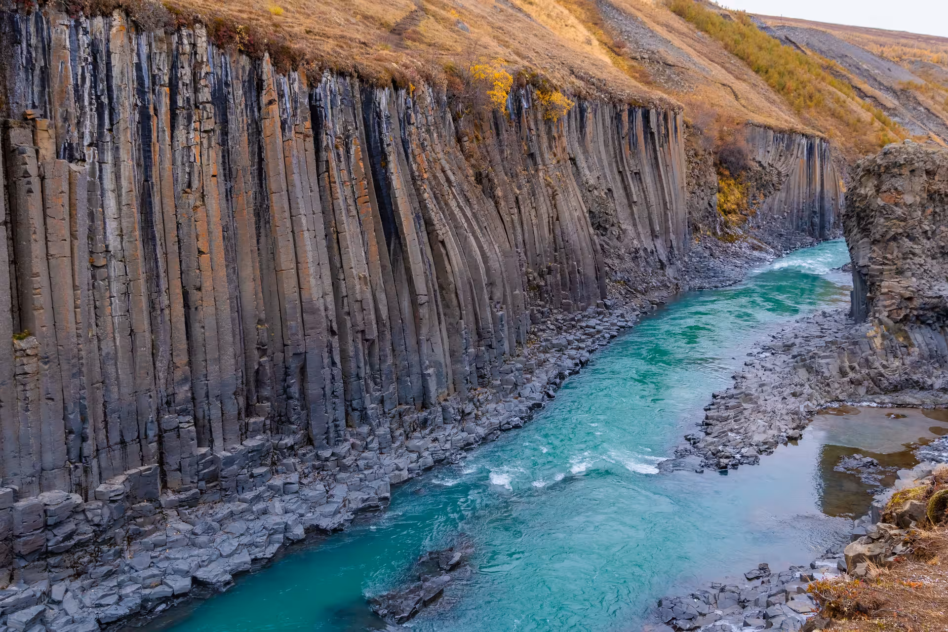 Studlagil Canyon with turquoise glacial river flowing between towering basalt column walls in Iceland