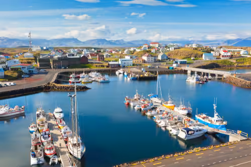 Aerial view of Stykkishólmur harbor with boats docked, colorful buildings, and snow-capped Snaefellsnes mountains