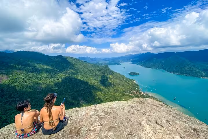Two adventurers enjoy stunning panoramic views from Peak Sugar Bread overlooking lush mountains and turquoise waters.
