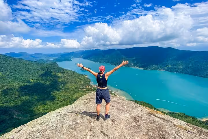 Adventurer embraces panoramic views from Peak Sugar Bread summit, showcasing breathtaking landscape and azure waters.