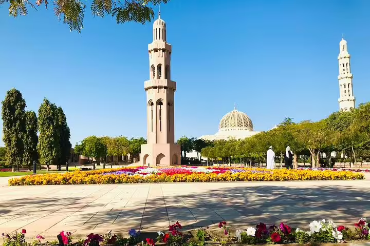 Vibrant garden scene at Sultan Qaboos Grand Mosque in Muscat, highlighting colorful flowers and towering minarets on a sunny day.