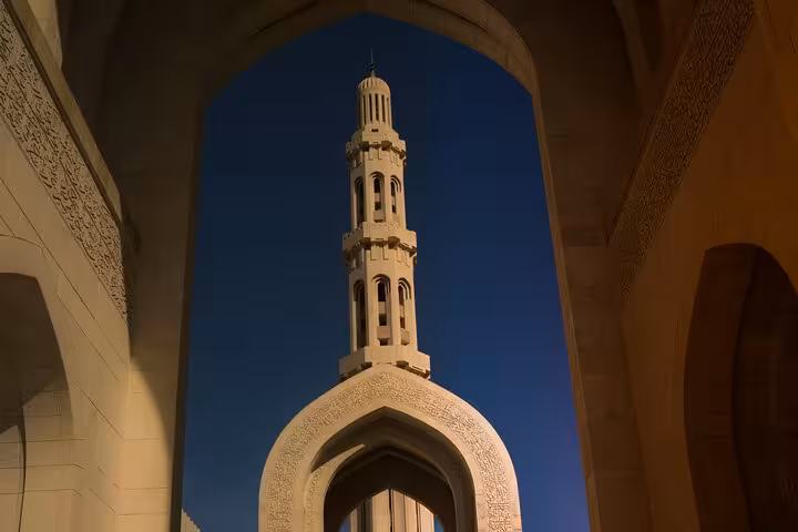 Elegant white minaret of Sultan Qaboos Grand Mosque framed by arches, visited on Muscat classic sightseeing taxi tours