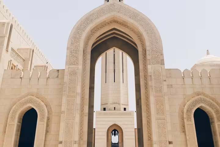 Close-up of ornate stone arches and central minaret at Sultan Qaboos Grand Mosque, a highlight of half-day Muscat city tours