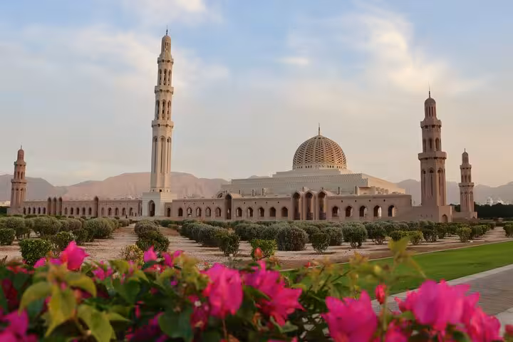 Sultan Qaboos Grand Mosque with towering minarets and vibrant pink flowers on a scenic Muscat city tour