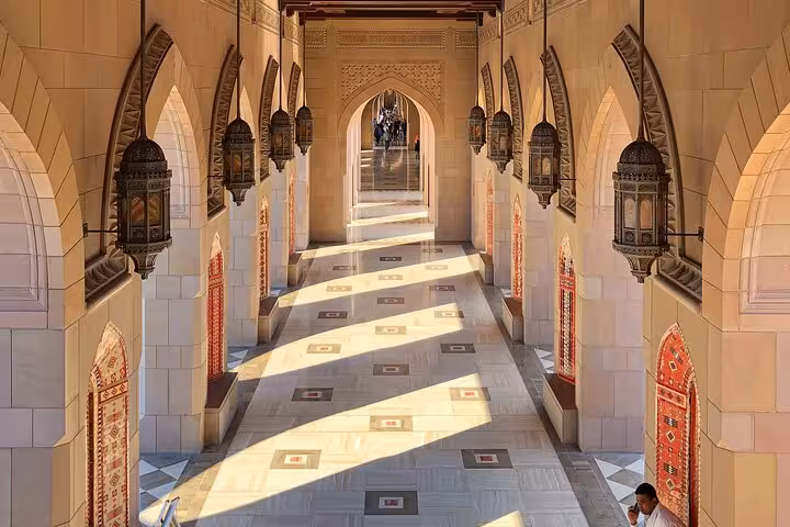 Sunlit arched corridor with ornate Islamic lanterns and mosaic floor tiles at Sultan Qaboos Grand Mosque Muscat tour
