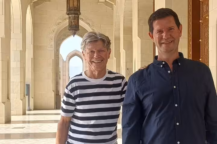 Two smiling visitors exploring the elegant marble corridors of Sultan Qaboos Grand Mosque on a guided tour in Muscat Oman.
