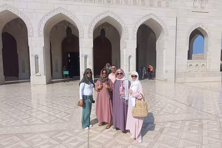 Tourists posing at Sultan Qaboos Grand Mosque marble courtyard during a guided tour in Muscat Oman