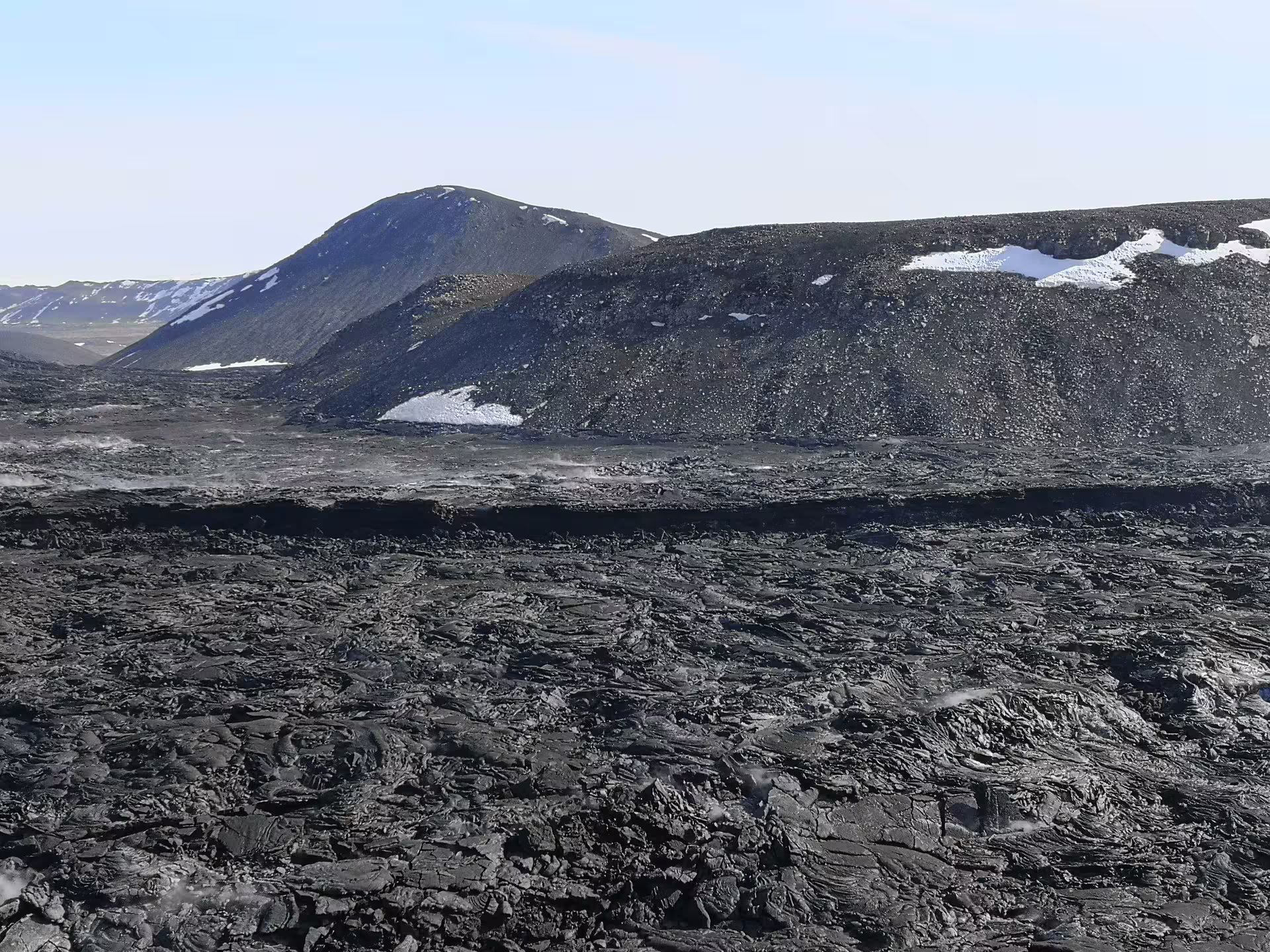Black hardened lava field with snow-dusted volcanic mountains at Sundhnjukar crater, Iceland