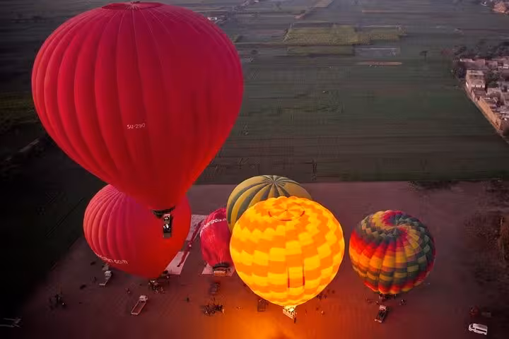 Sunrise hot air balloons inflating over Luxor farmlands, Egypt, with hotel pickup & drop-off balloon ride tour