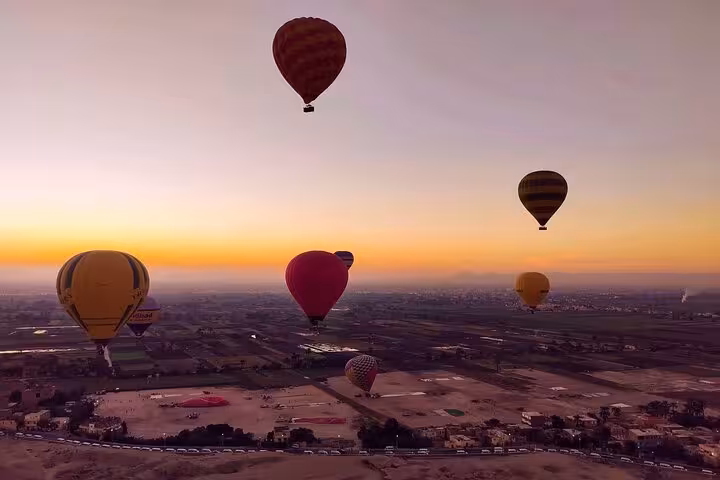 Hot air balloons soar at sunrise over Luxor's West Bank, offering a breathtaking aerial view of the ancient landscape.