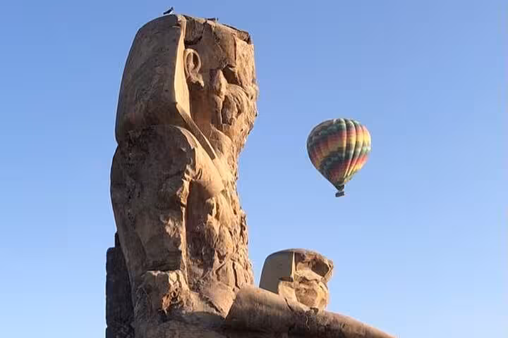 Majestic hot air balloon soaring near ancient statues on Luxor West Bank during a sunrise tour.