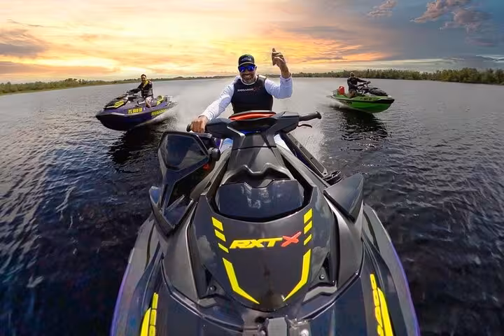 Three riders on jet skis at sunrise on calm water, front rider on Sea-Doo RXT-X waving