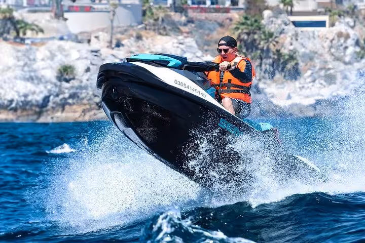 Rider in orange life jacket performing jet ski jump on blue sea near rocky coastline