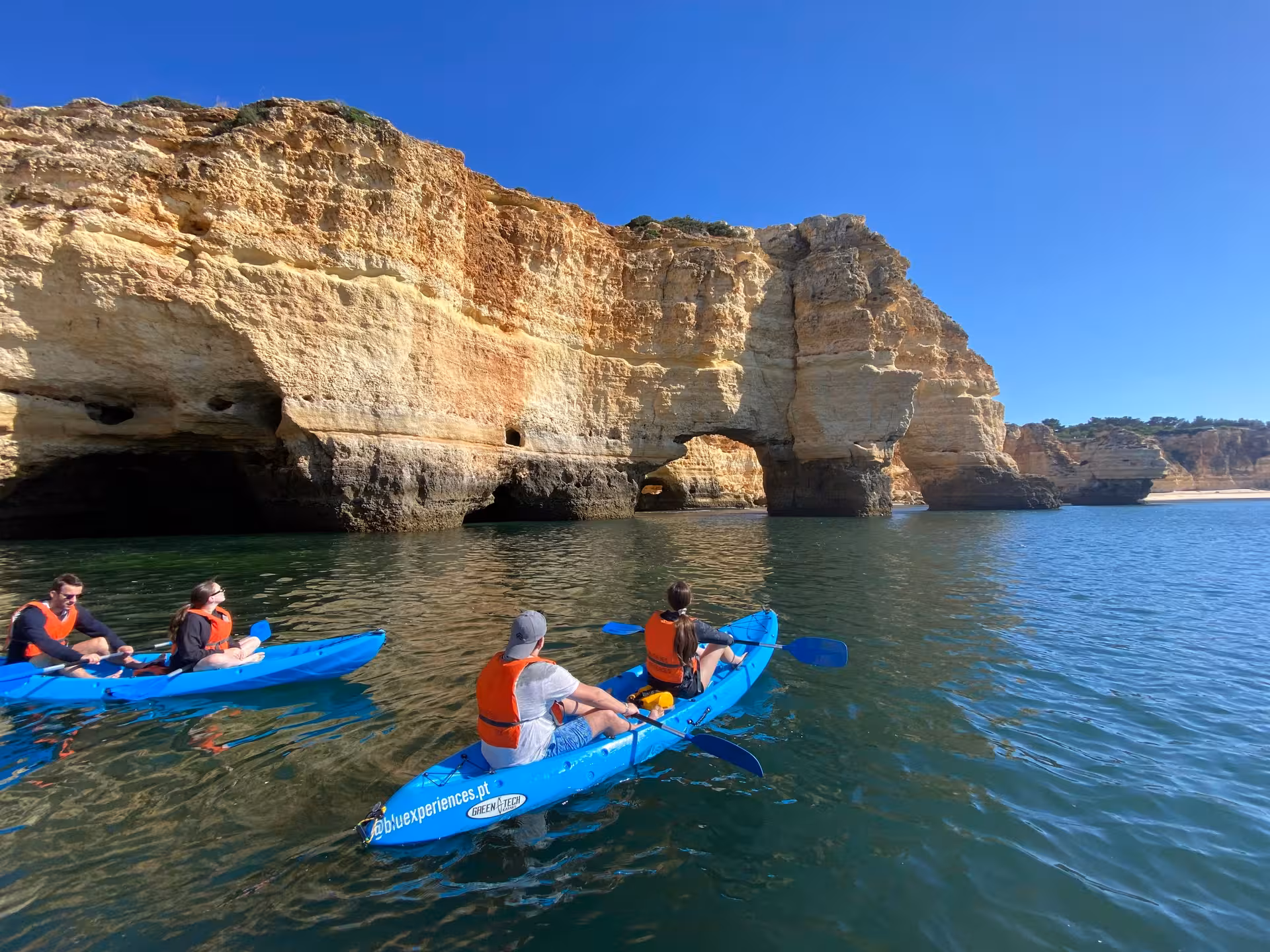 Small group sunrise kayak tour gliding toward Benagil sea caves and golden Algarve cliffs on calm Atlantic waters in Portugal
