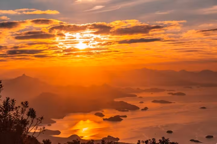 Vibrant sunrise over Pedra da Macela, illuminating the ocean and islands with a warm orange glow.