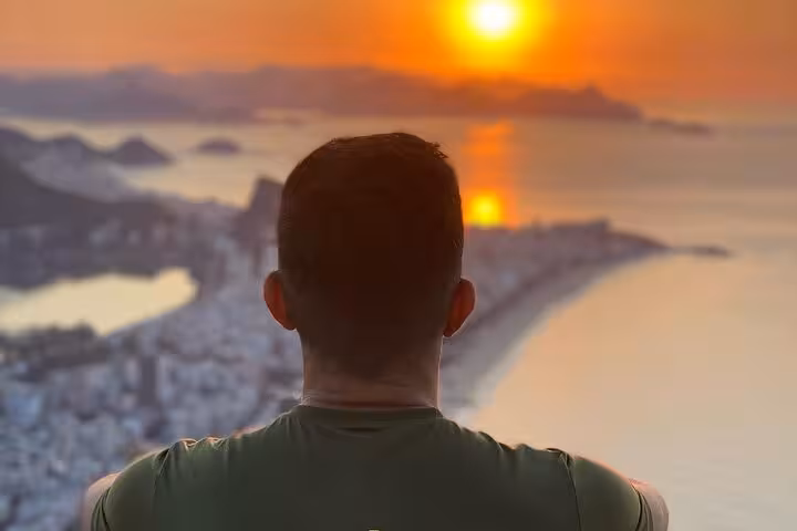 Person admiring breathtaking sunrise over Rio de Janeiro from a high vantage point with vibrant orange sky.