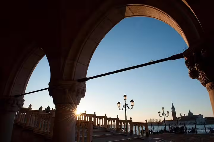 Sunrise view through Venetian arches with lamp posts and a distant church, perfect for an early morning photo tour.