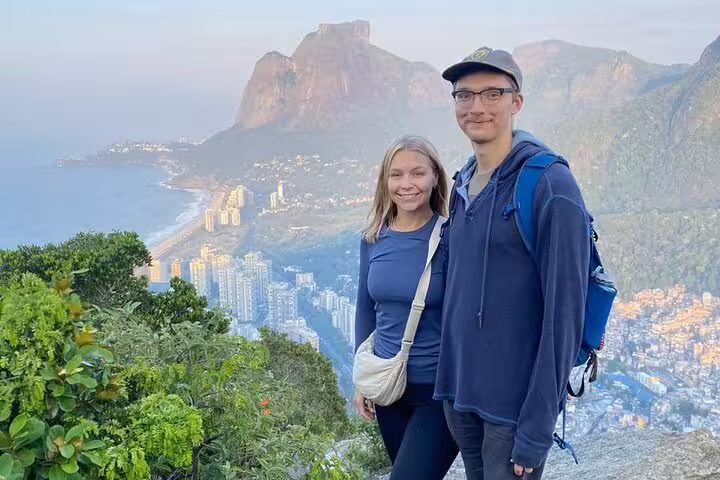Couple posing at sunrise on Two Brothers Peak with panoramic views of Rio de Janeiro's coastline and mountains.