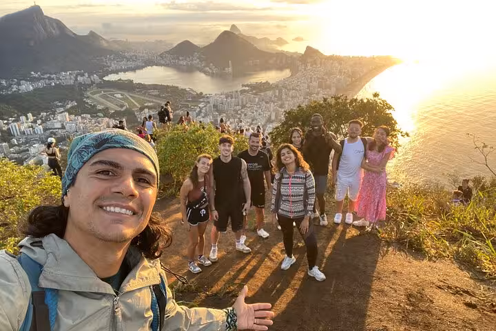 Smiling group with guide on a sunrise walk at Two Brothers peak, overlooking stunning Rio de Janeiro vistas.