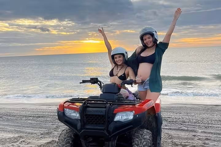 Two riders on ATV at Jericoacoara beach during sunset, guided quad bike tour with helmets and sea backdrop