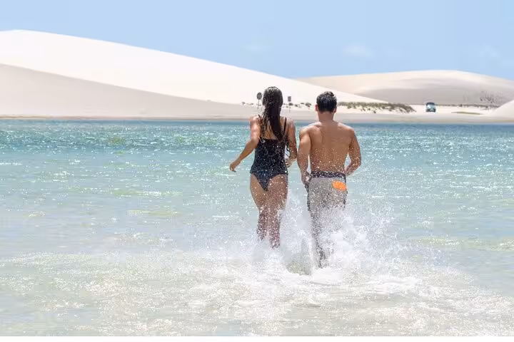 Two travelers wading into turquoise lagoon with dunes behind, scenic stop on Jericoacoara sunset ATV tour