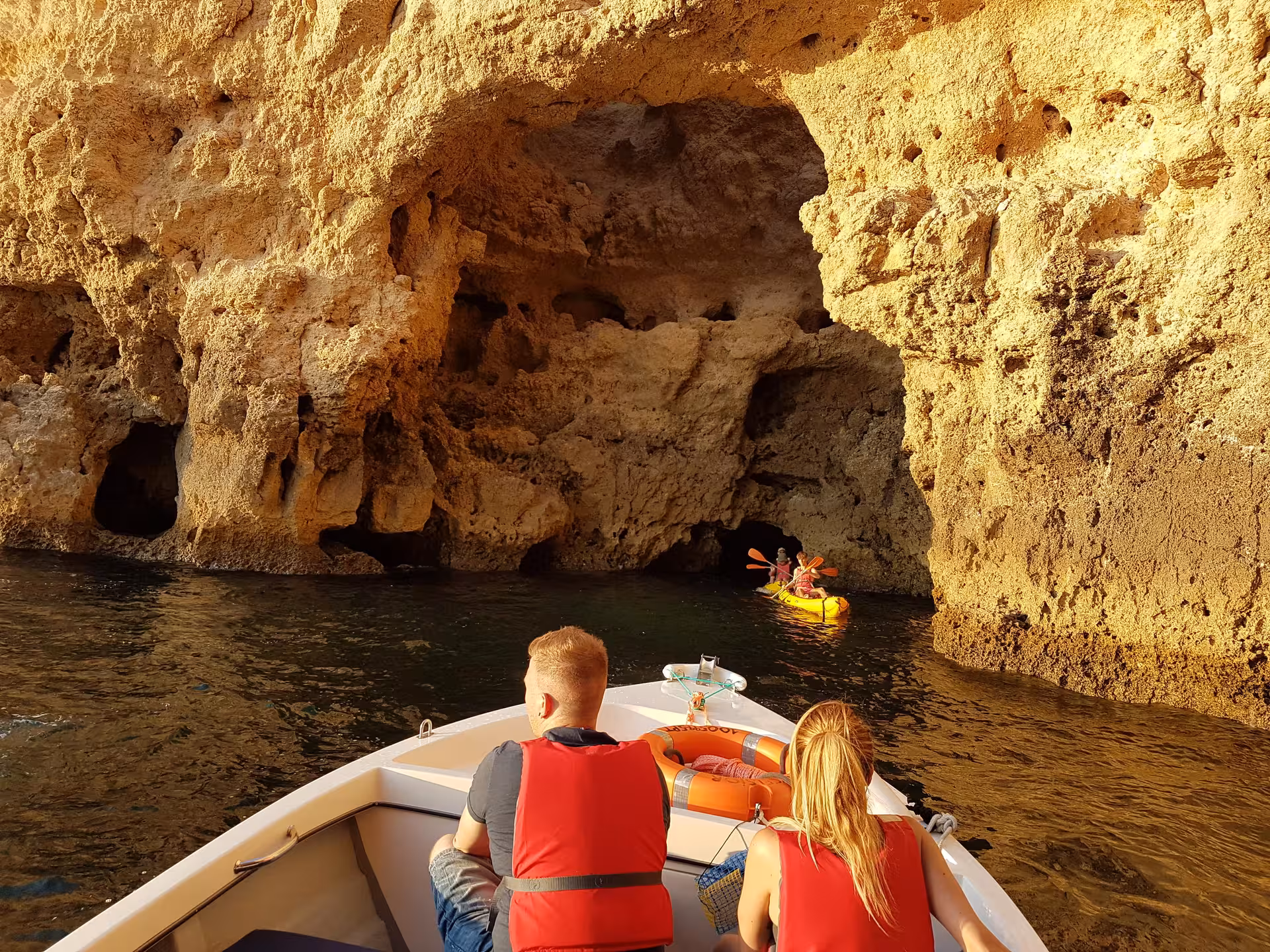 Guests in life jackets cruise by kayakers exploring golden sea caves at Ponta da Piedade near Lagos, Algarve