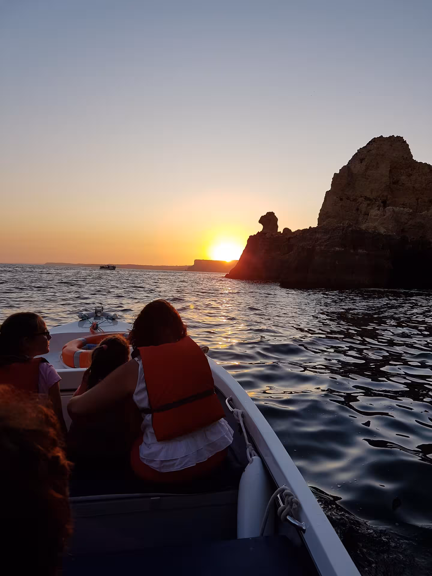 Family wearing life jackets on a sunset boat trip at Ponta da Piedade in Lagos, passing golden cliffs and shimmering sea