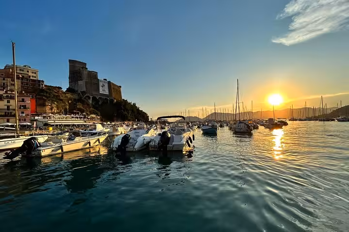 Sunset view of boats docked in a serene Cinque Terre harbor with a historic castle on the hill.