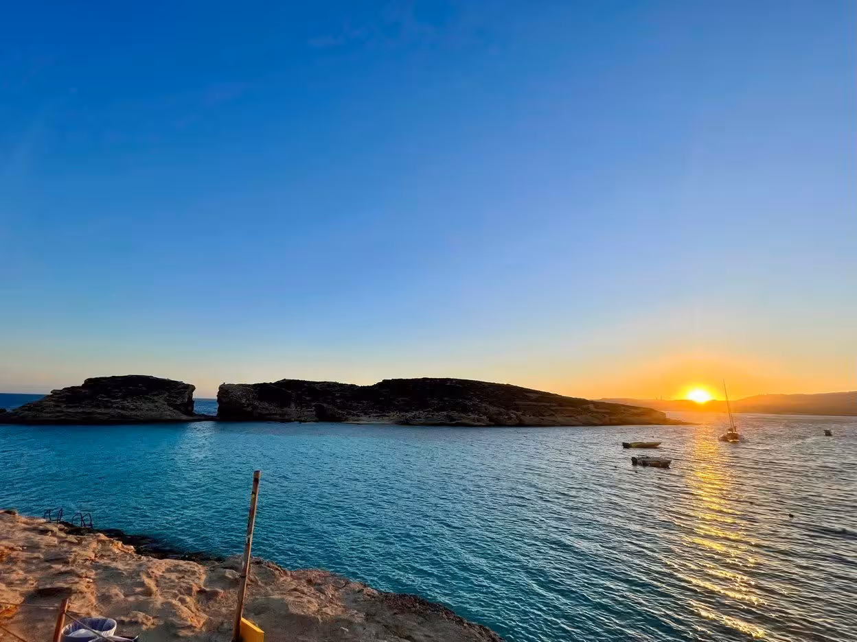 Sunset over Comino Blue Lagoon, Malta, with boats on calm water during Blue & Crystal Lagoons tour