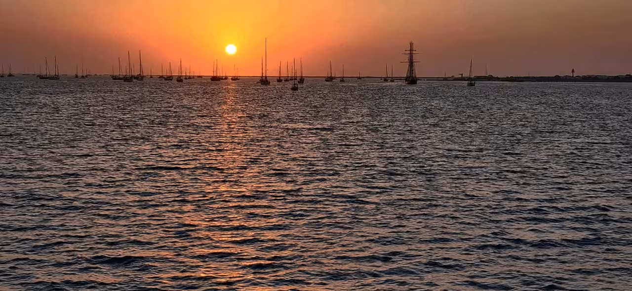 Golden sunset cruise view over calm sea with sailboats and a tall ship, perfect for an evening sunset tour