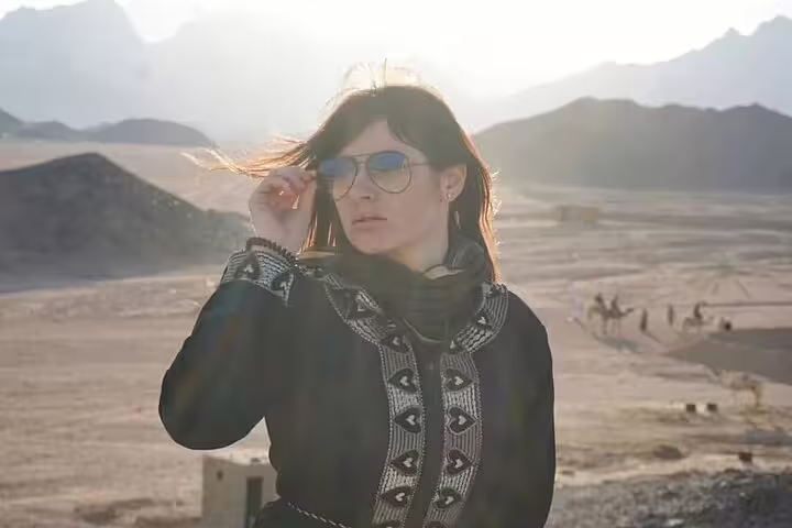 Traveler in sunglasses at golden hour in Marsa Alam desert, sunset safari experience with ATV quad and camel ride
