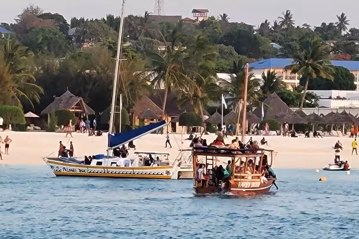 Tourists on a dhow and a sailboat near Kendwa beach, enjoying a sunset cruise in Zanzibar.