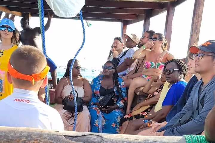 Group of tourists relaxing on a dhow during a sunset cruise in Zanzibar's serene waters.
