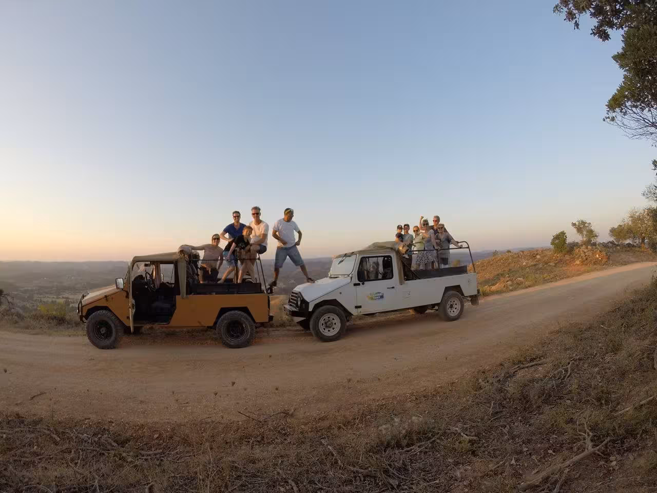 Group sunset jeep tour in the Algarve countryside, guests standing on 4x4s with sparkling wine and golden views