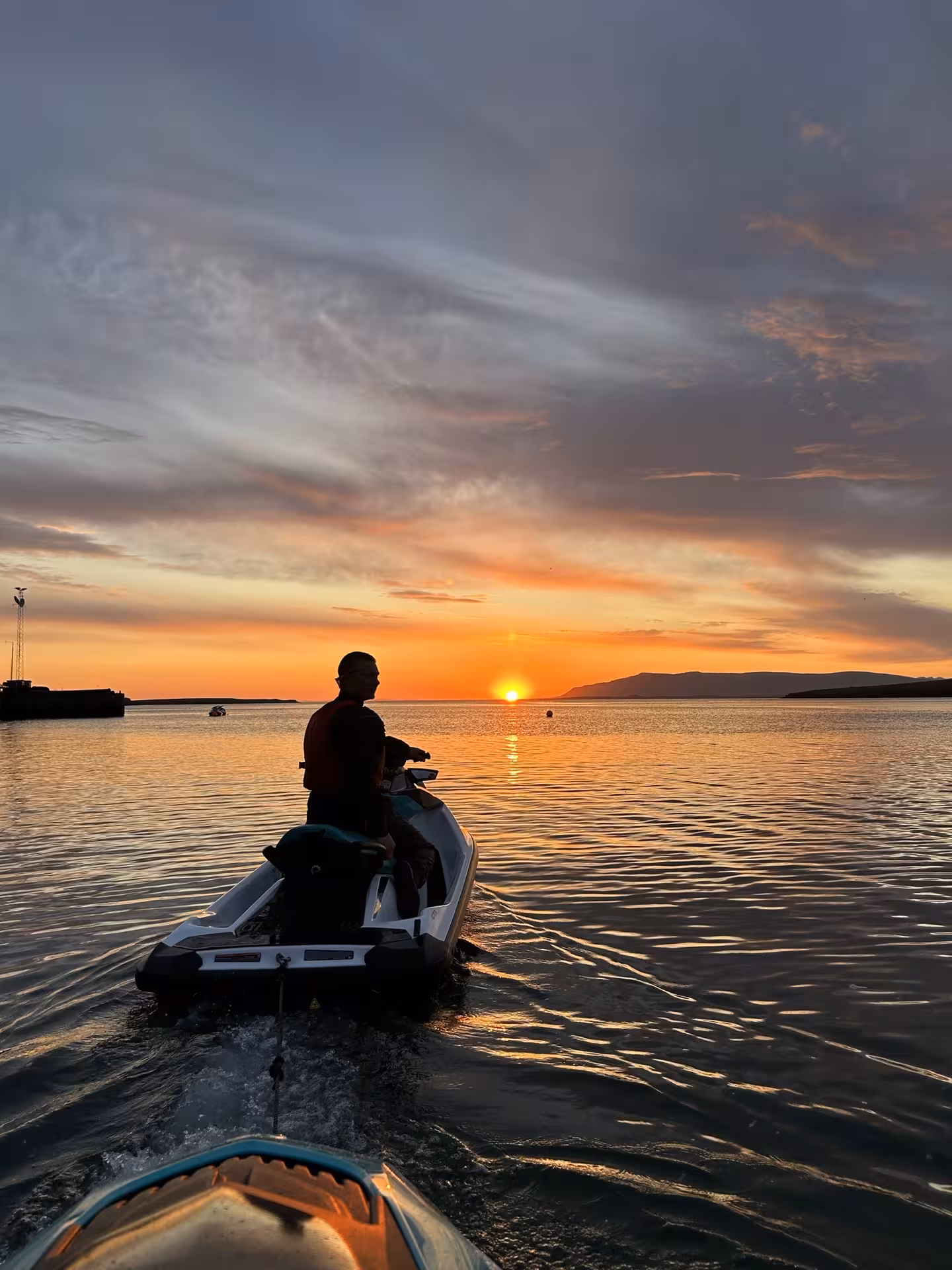 Person on jet ski silhouetted against a vibrant orange sunset over the Bay of Reykjavik