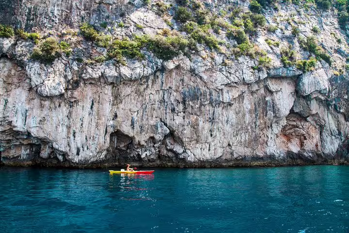 Sea kayaks beside dramatic coastal cliffs over clear blue water, a sunset kayaking and snorkeling tour with wine