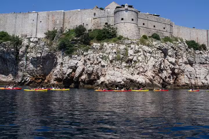 Sea kayaks glide below Dubrovnik city walls and cliffs, part of a sunset kayaking and snorkeling tour with wine