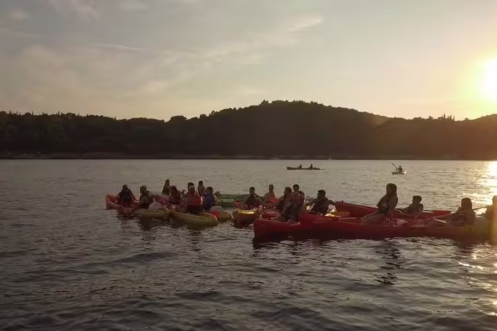 Kayakers gather at golden hour on the bay, enjoying sunset kayaking and snorkeling tour with water and wine