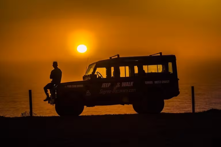 Silhouette of a person and jeep against a vibrant sunset backdrop during a West Coast off-road adventure.