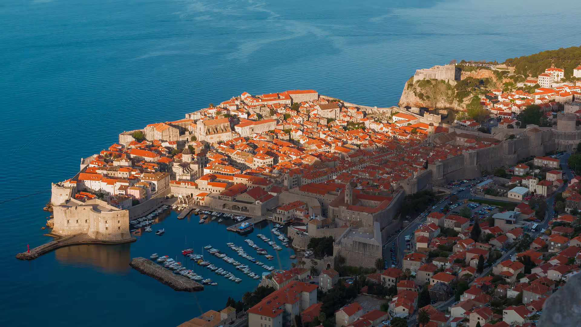 Panoramic sunset view of Dubrovnik city walls, Old Town rooftops and marina on scenic coastal drive