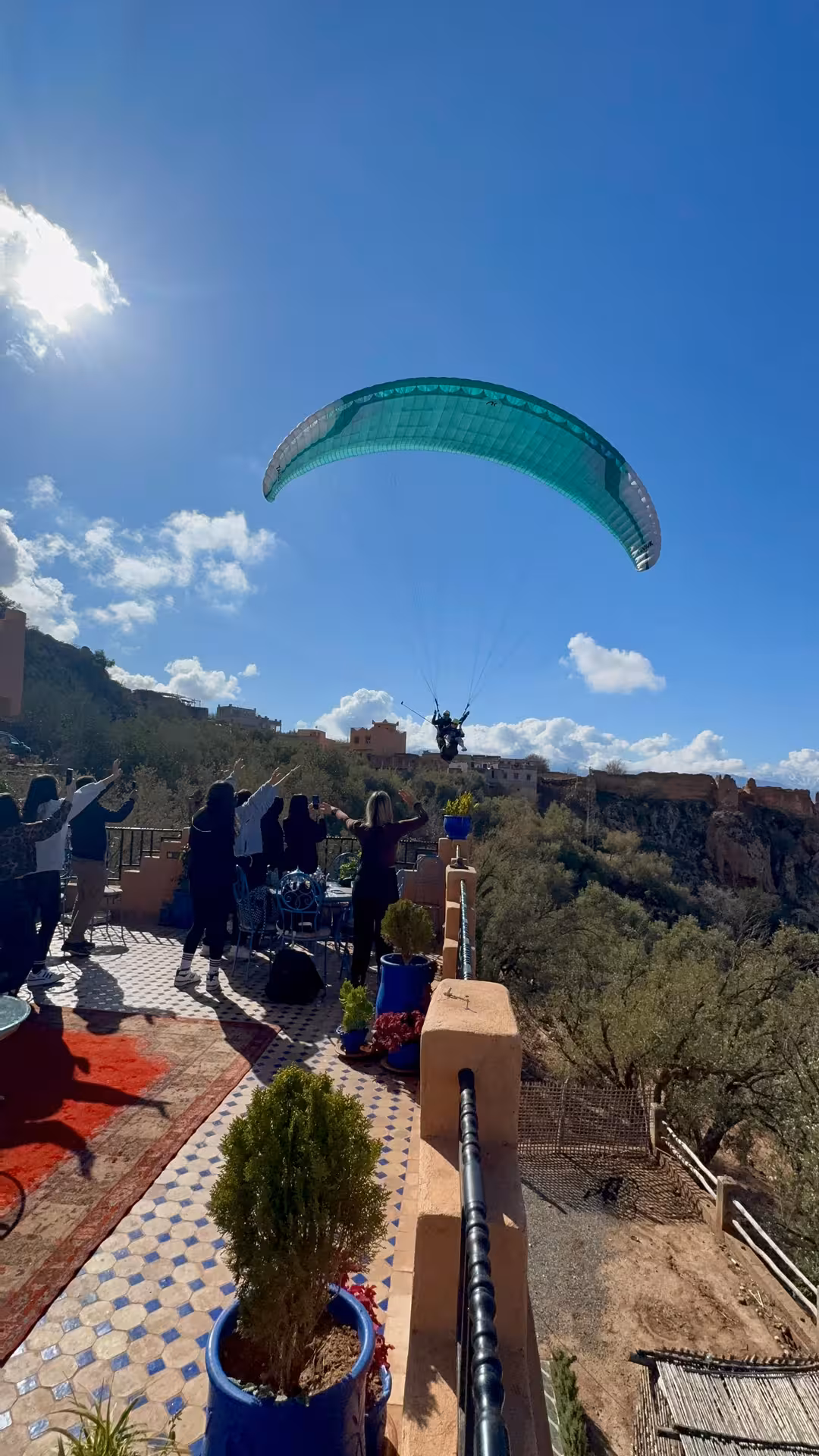 Paraglider soaring above the Agafay Desert as onlookers cheer from a scenic terrace.
