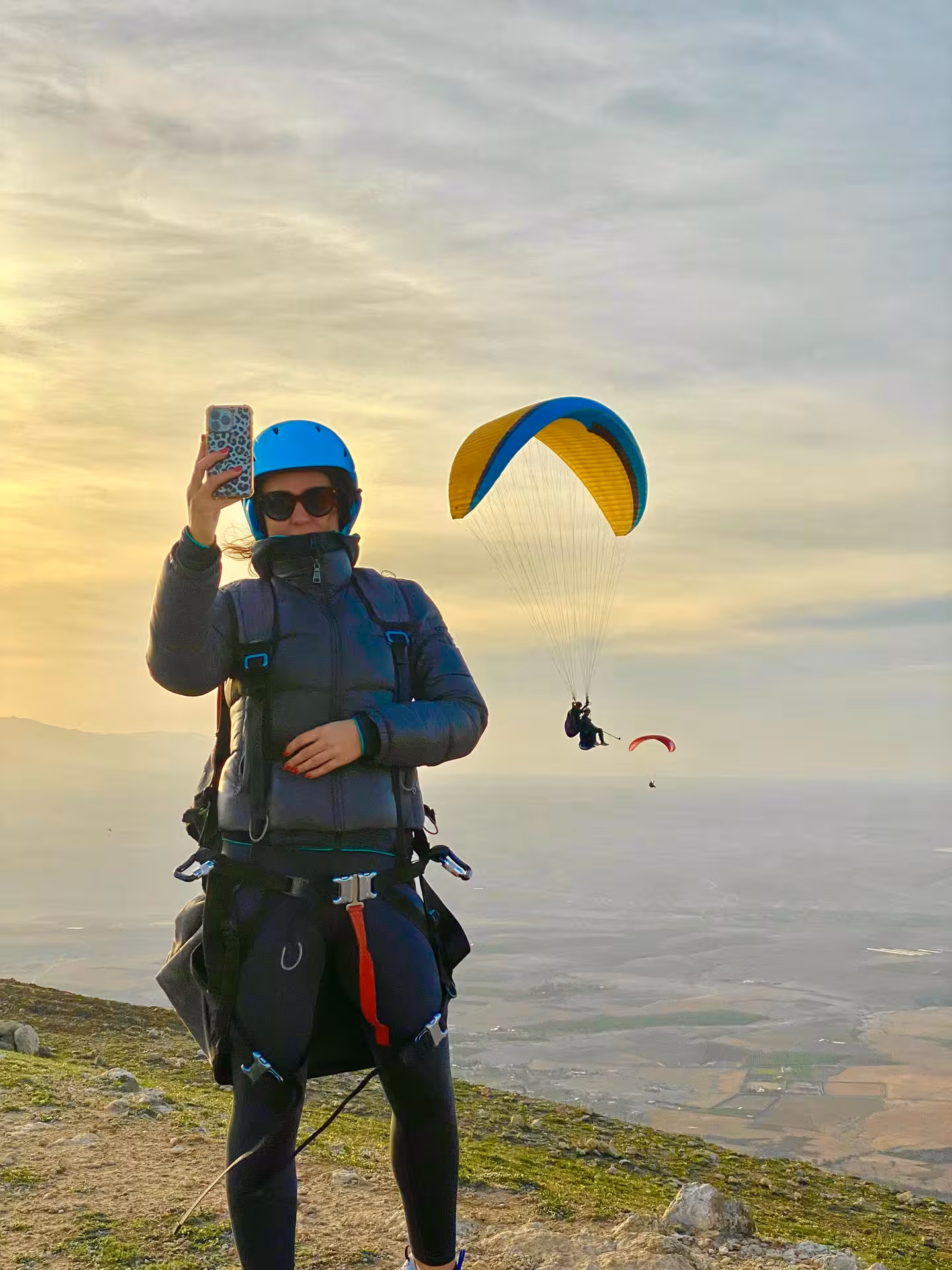 Woman capturing a selfie before a paragliding flight at sunset over the Agafay Desert near Marrakech.