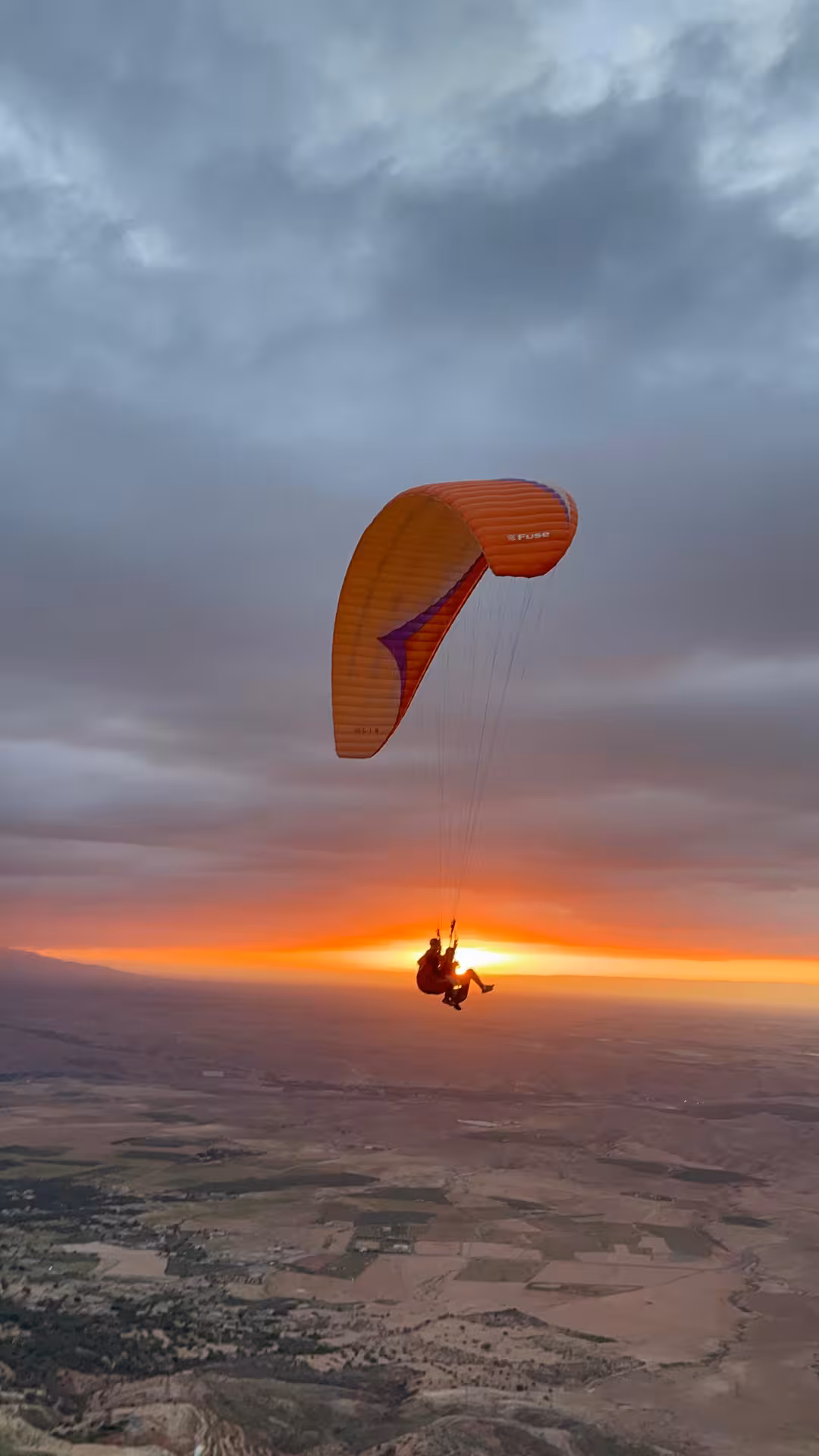 Paraglider soaring over Agafay Desert at sunset, capturing the vibrant orange hues from Marrakech.