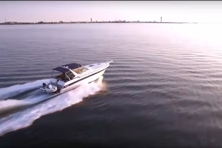 Private yacht cruise at sunset speeding across calm sea, aerial view with golden light and wake trail