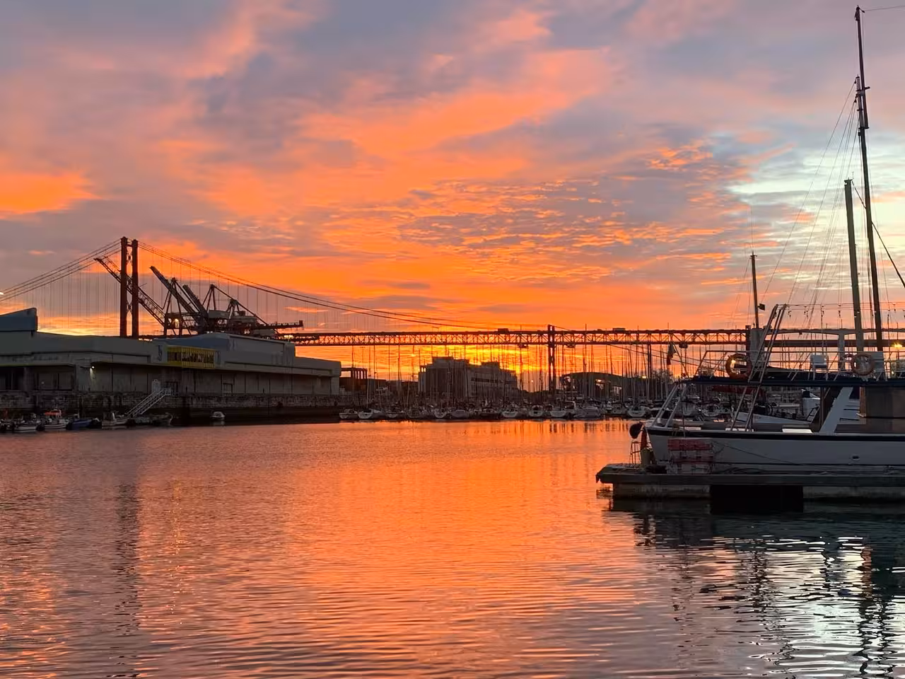 Colorful sunset over Lisbon marina and 25 de Abril Bridge, captured from dock before shared Tagus River sailboat tour