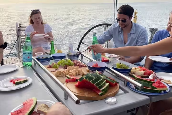 Guests enjoying a sunset sailing experience with an open bar and tapas, featuring fresh fruit and drinks on a yacht.